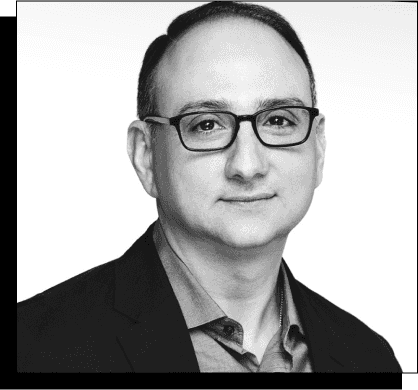 Professional headshot of agency partner Tom Di Domenico, wearing glasses, a professional collared shirt, and a black jacket