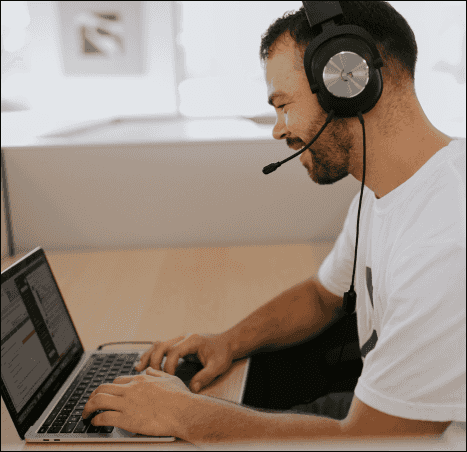 A Nexcess support agent in a headset smiles as he types on a laptop, the screen shows a migration process for websites